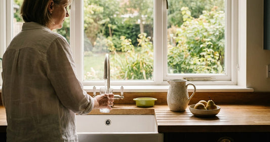 Woman filling a water glass at a bright kitchen window in late summer — Desert Harvest