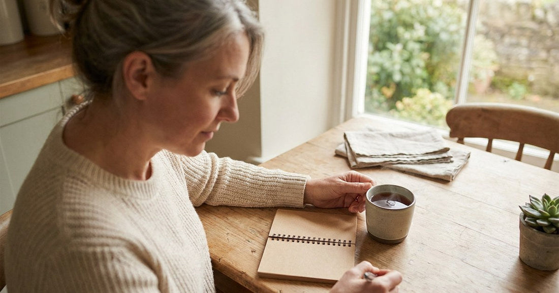 Woman writing in a notebook at her kitchen table while preparing for a doctor's appointment