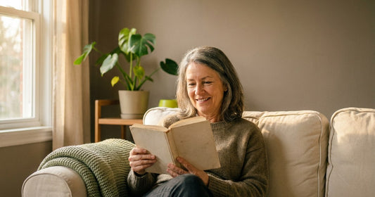 Woman in her 60s reading on a sofa, a Desert Harvest menopause wellness lifestyle scene