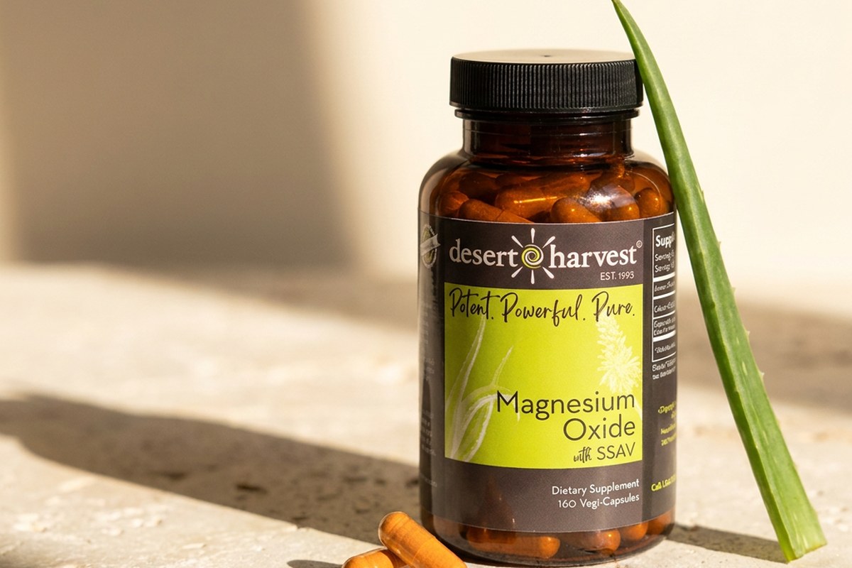 Desert Harvest Magnesium bottle with Aloe Vera leaf and capsules on pale stone in warm light